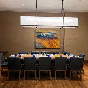 Private dining room with a long table, chairs, place settings, and a painting of a mountain on the wall.